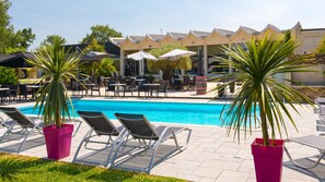 Un espace aménagé au bord de la piscine, avec des chaises longues, des parasols et un bâtiment dont le toit a une forme particulière.
