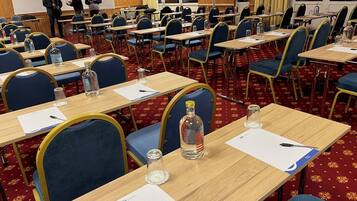 Un salón de conferencias con filas de mesas, sillas y una pantalla para proyector.