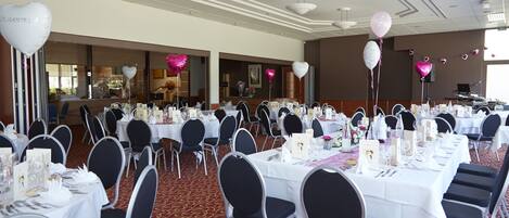 A banquet hall with round tables set for dining, white tablecloths, and black chairs.