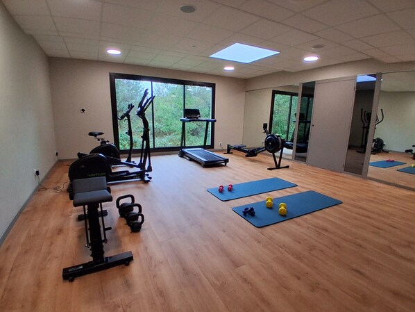 Une salle de sport équipée de matériel d’exercice, de tapis et dotée d’une fenêtre donnant sur des arbres.