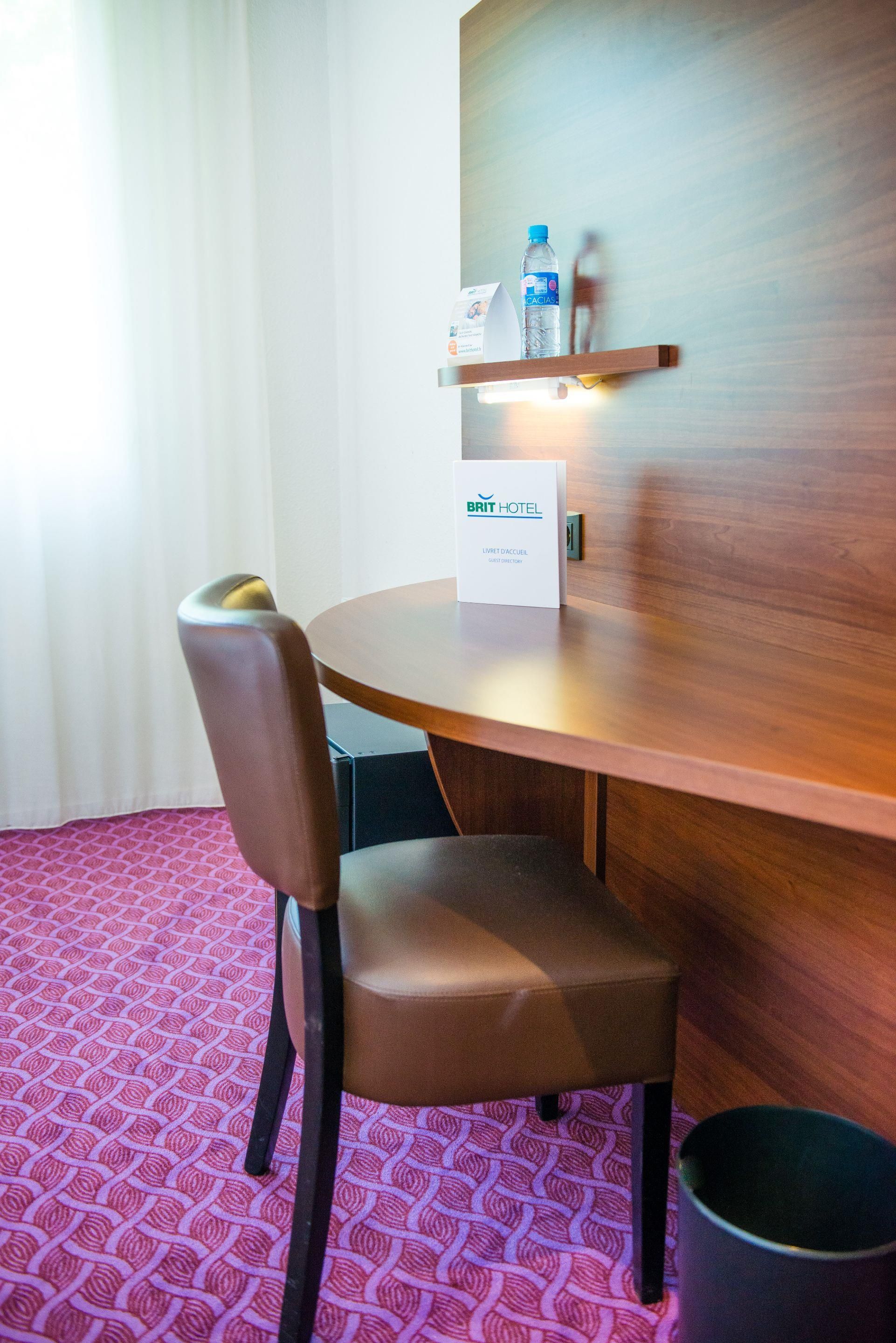 Une chambre d’hôtel avec une table en bois, une chaise, une bouteille d’eau et un guide d’information pour les clients posé sur la table.