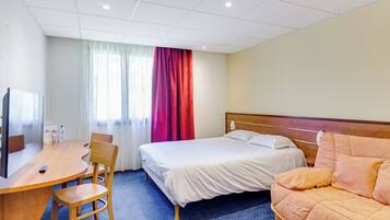 A hotel room with a bed, a sofa, a desk with a chair, a television, and a window with curtains.