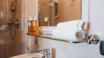 Un bagno con box doccia in vetro, un porta asciugamani con un asciugamano piegato e uno scaffale con articoli da toilette.