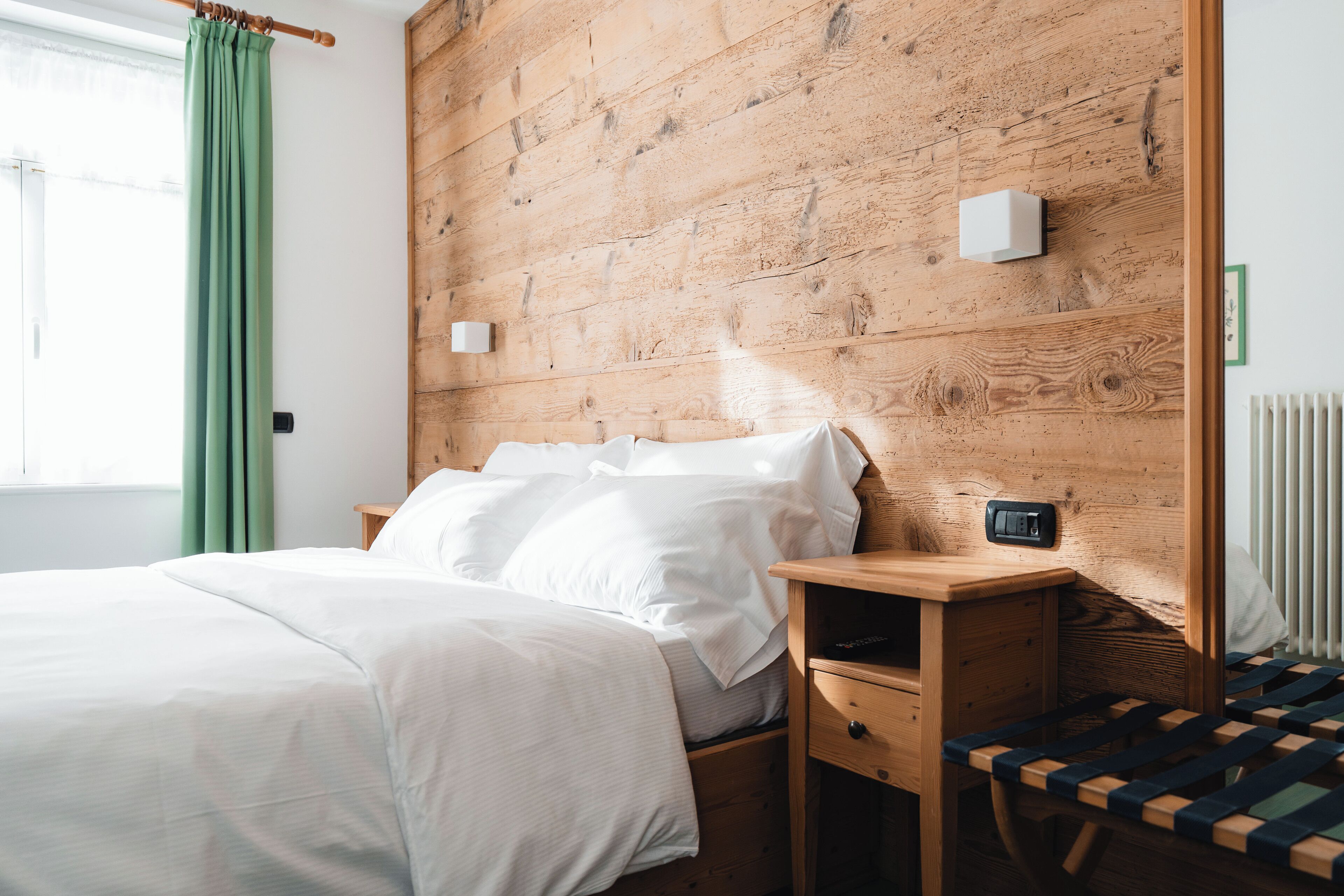 A neatly made bed with white linens, a wooden nightstand with a drawer, and a small bedside table with a lamp.