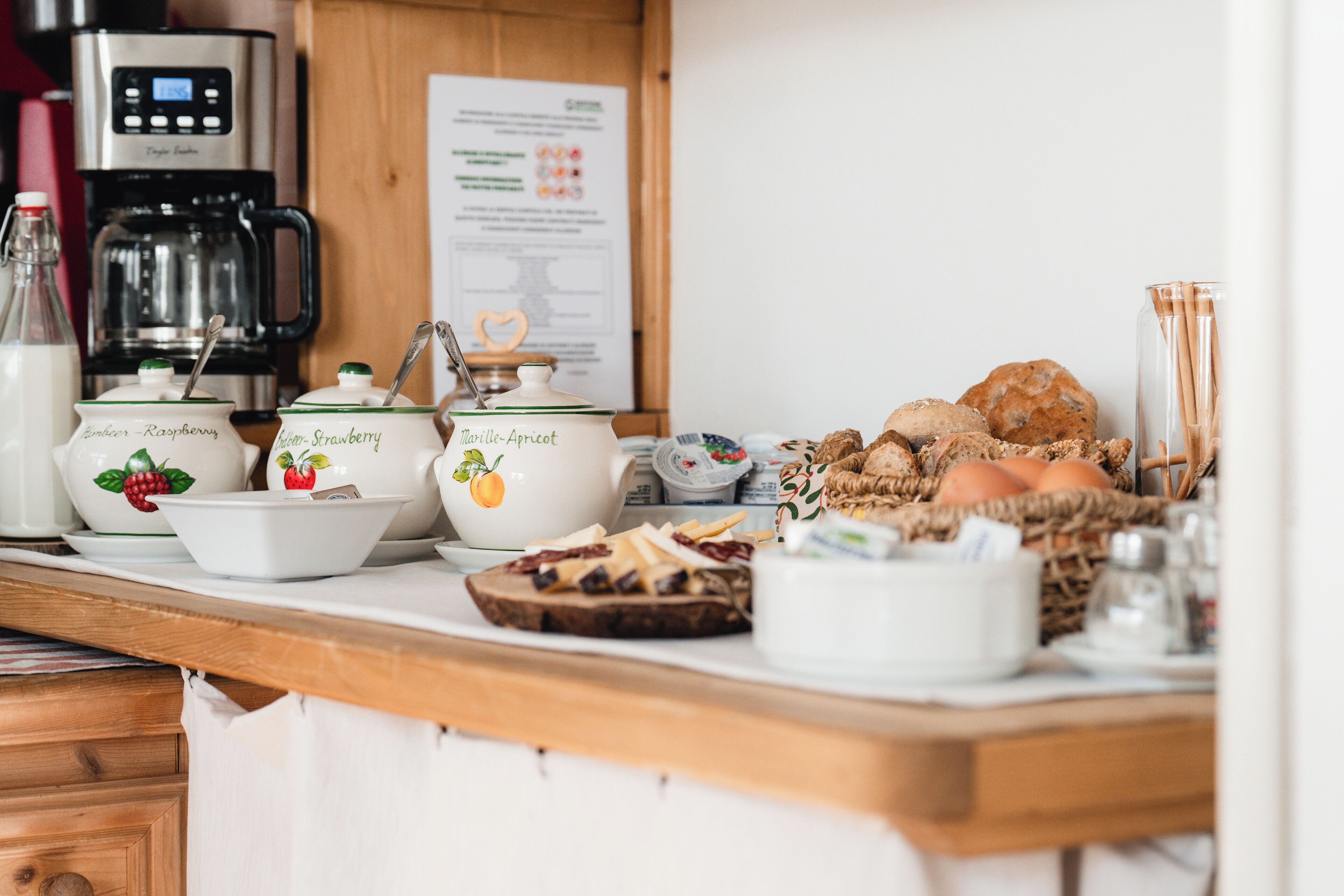 A breakfast buffet with various food items and containers, a coffee maker, and a menu board in the background.