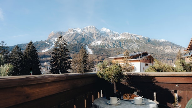 Une terrasse en bois avec une table dressée pour deux personnes, offrant une vue sur une chaîne de montagnes et une piste de ski.