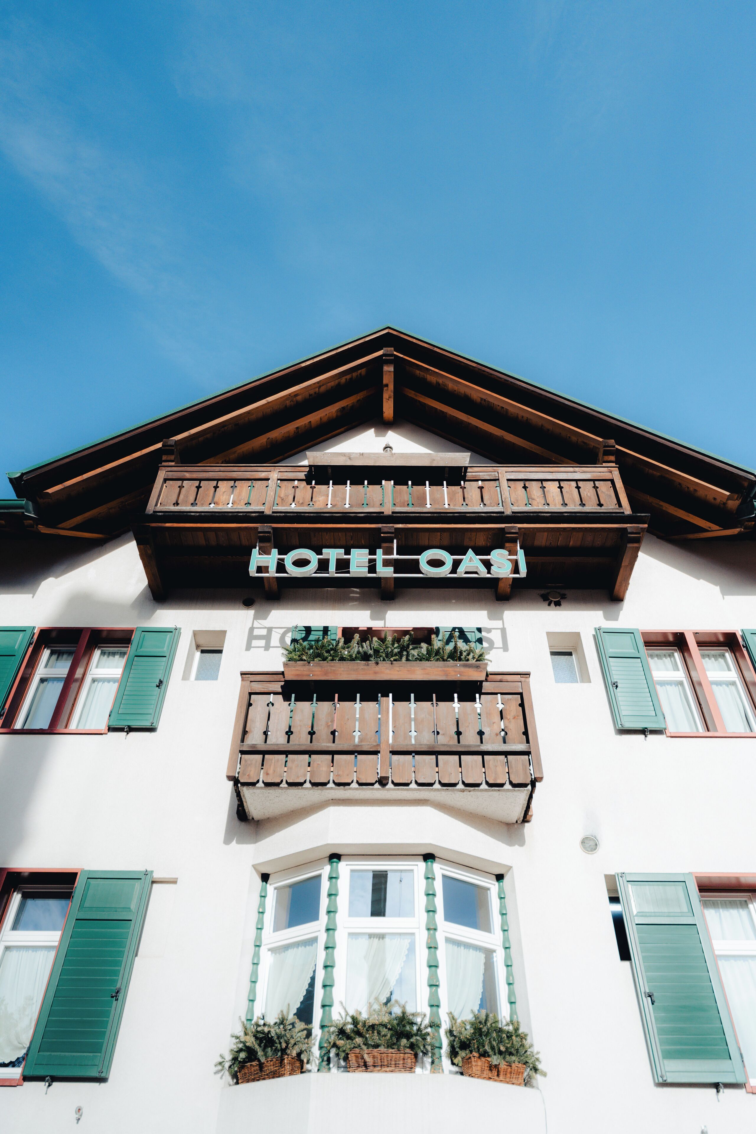 Ein Hotel mit der Aufschrift "HOTEL OASI", das traditionelle alpine Architektur mit Holzbalkonen und grünen Fensterläden aufweist.