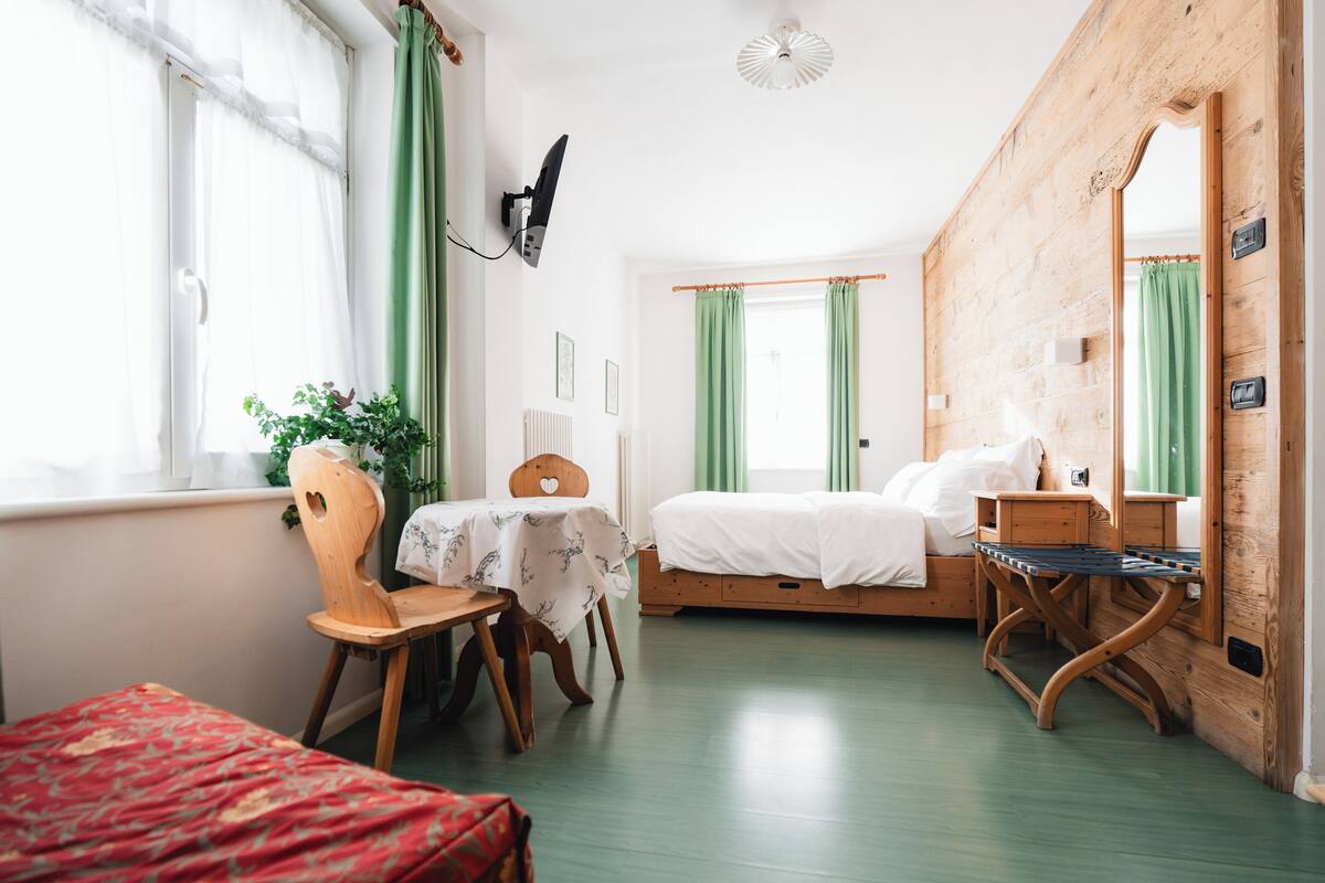 A room with a bed, a chair, a table, and a mirror.