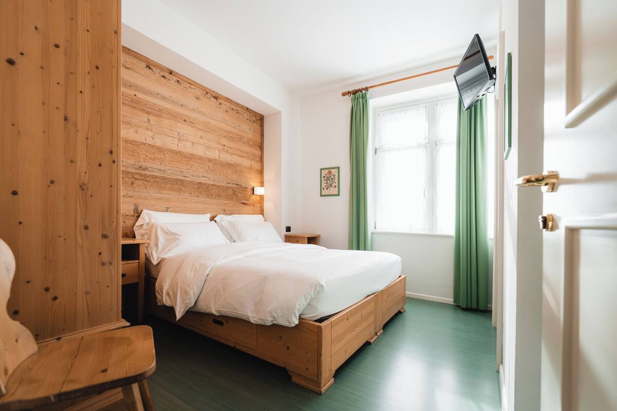 A bedroom with a wooden headboard, a bed with white linens, a green curtain, and a mounted television.