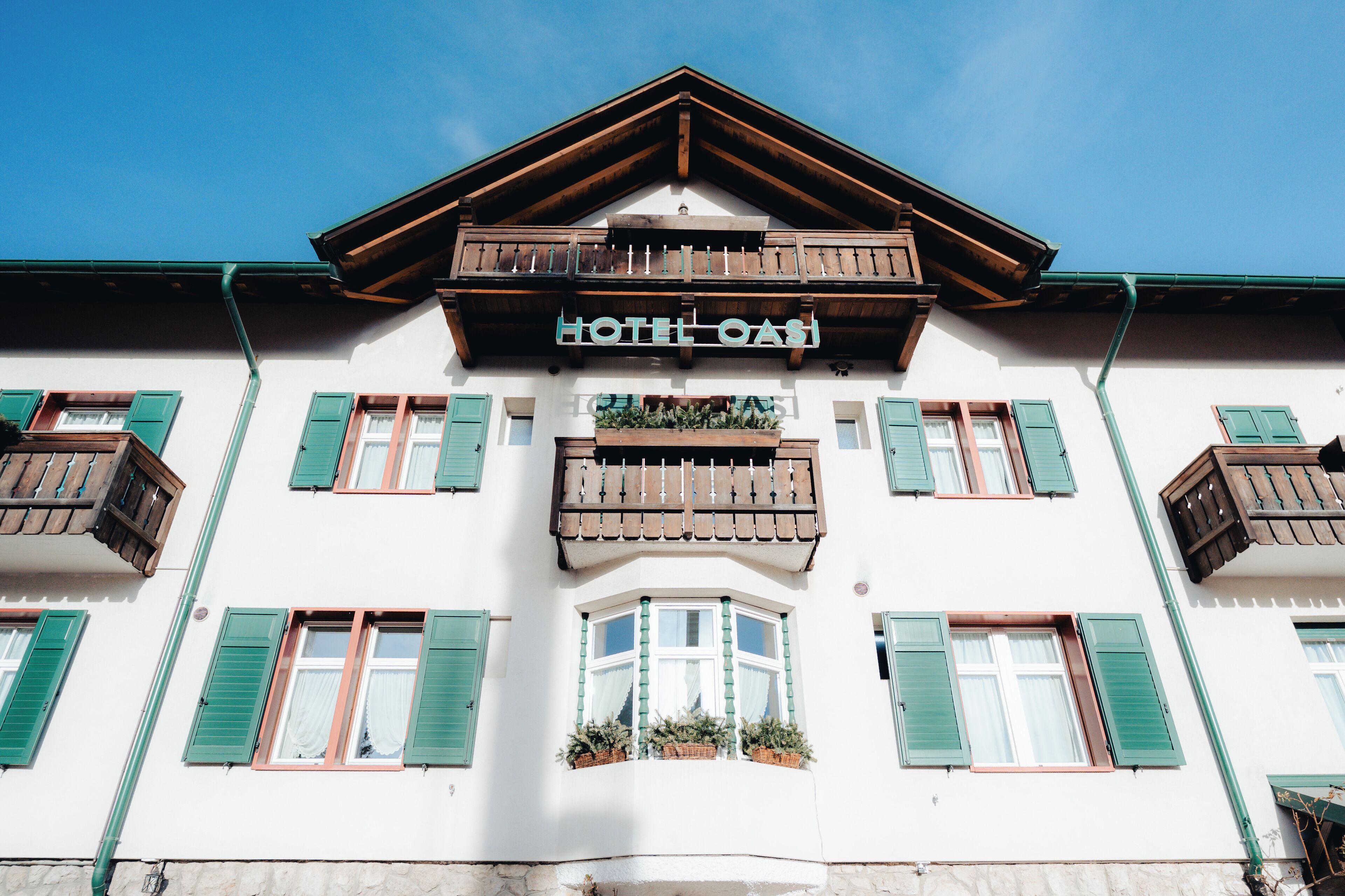 A hotel with a white facade, green shutters, and a balcony with wooden railings.