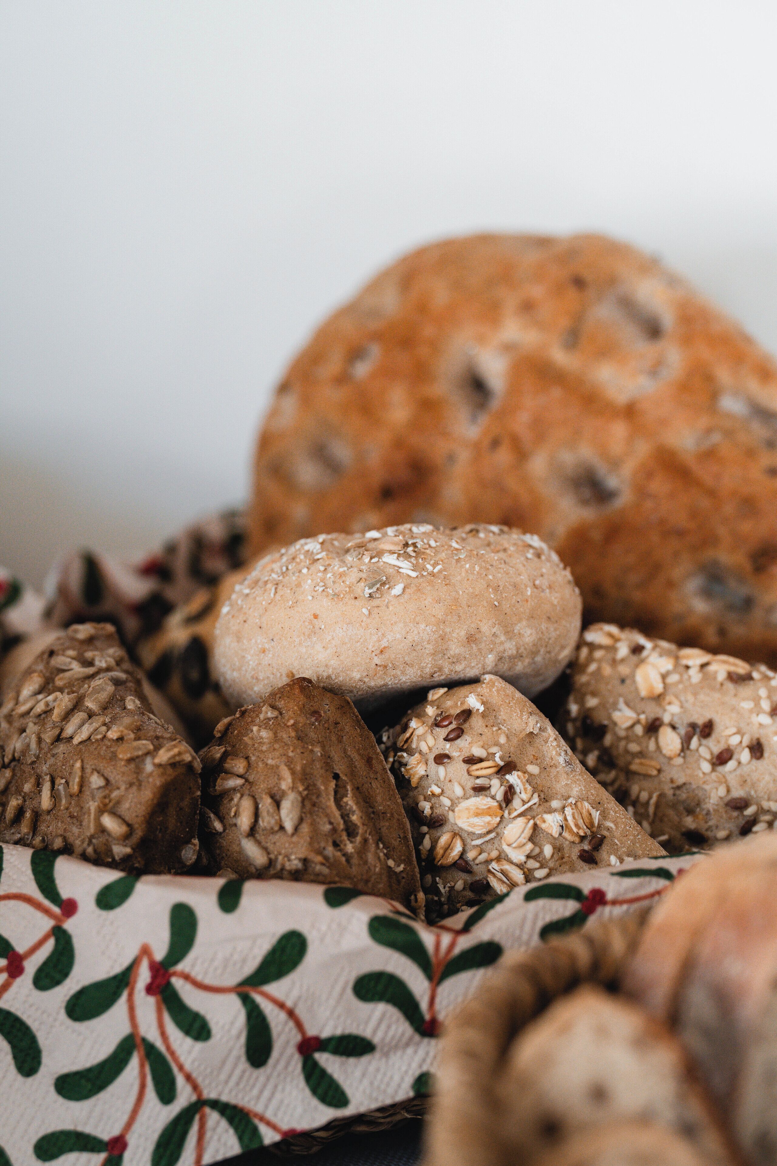 A variety of breads and rolls, some with seeds and grains, displayed on a cloth with a leaf pattern.