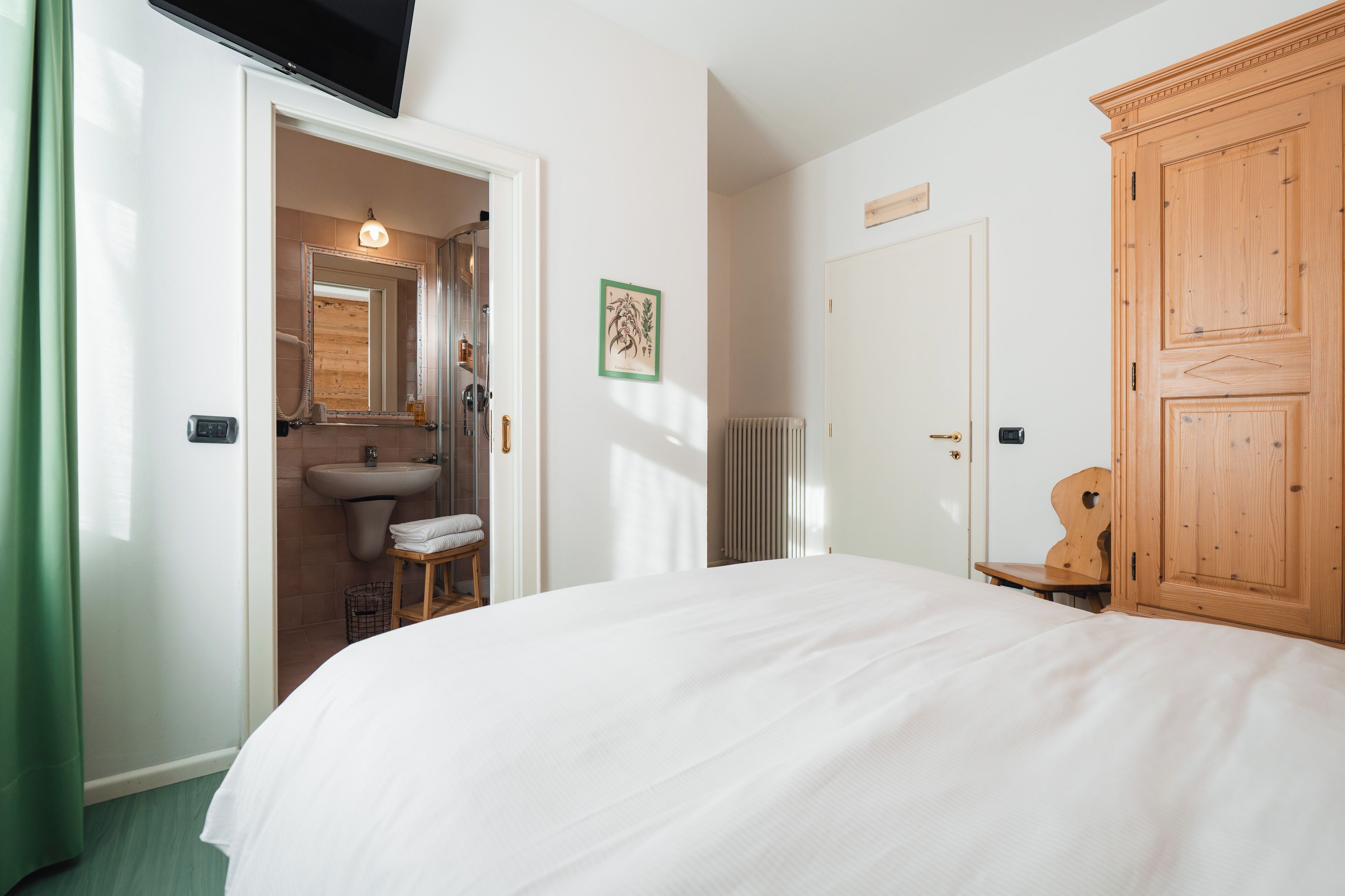 A bedroom with a bed, a wooden wardrobe, a bathroom with a sink, and a mirror.