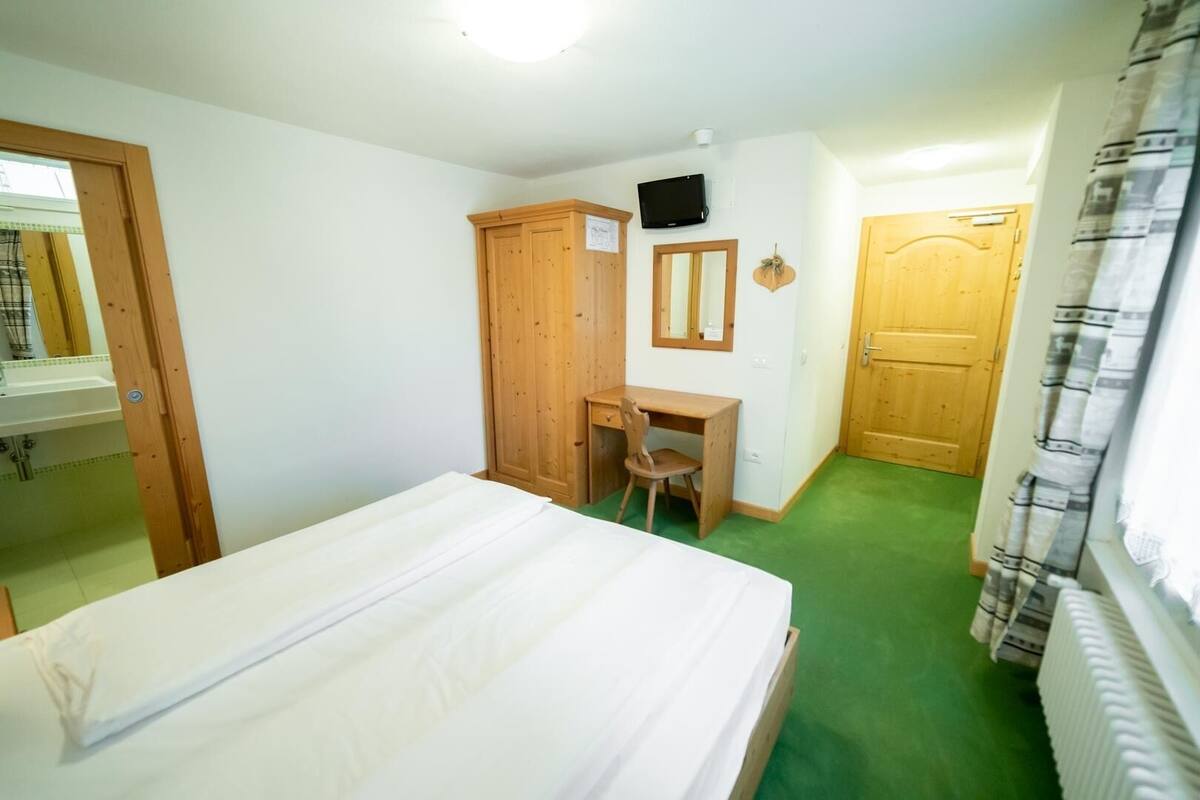 Un dormitorio con cama, escritorio, silla, armario, televisor y puerta.