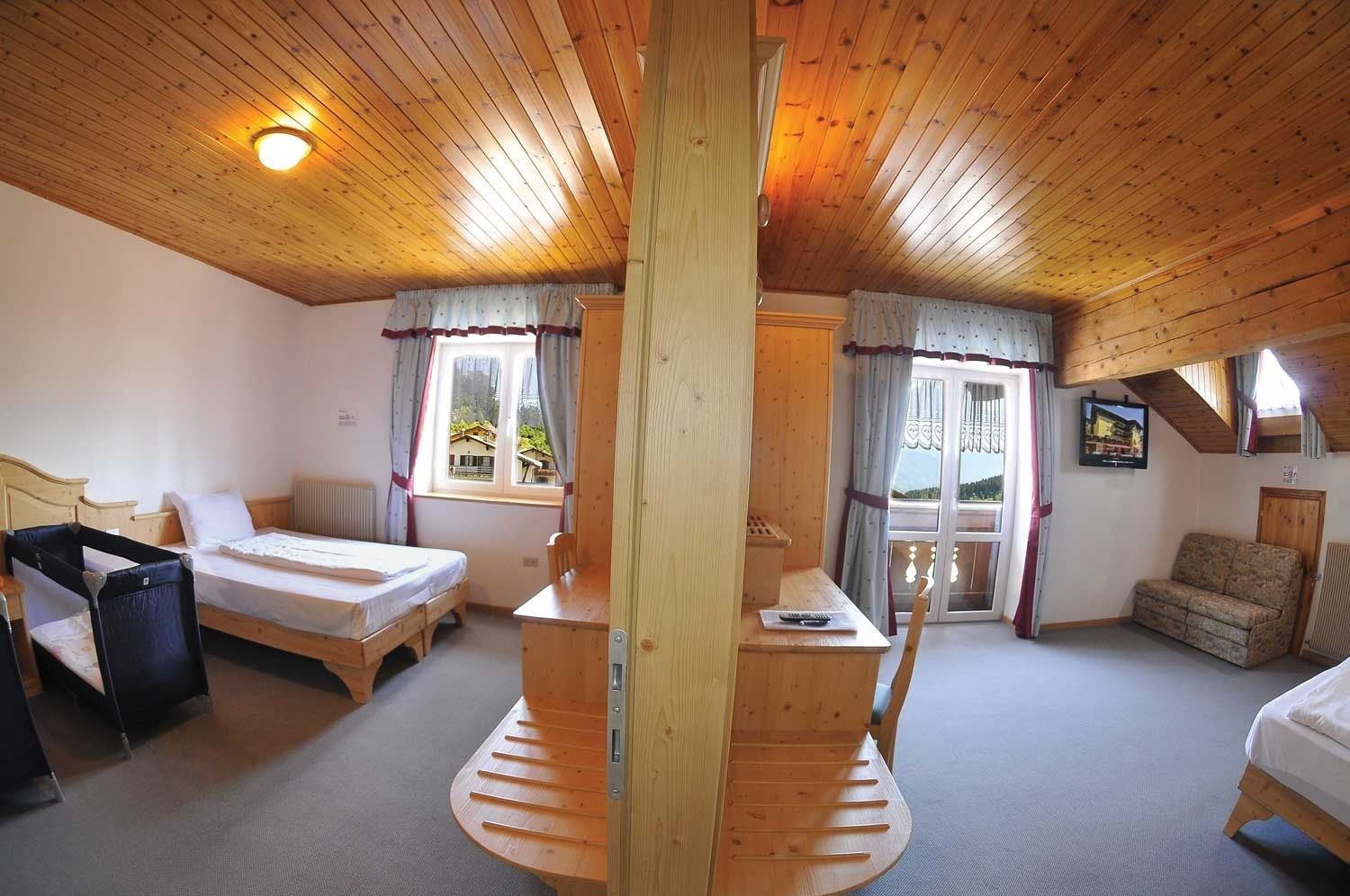 A cozy room with a wooden ceiling, a bed, a desk, and a sofa.