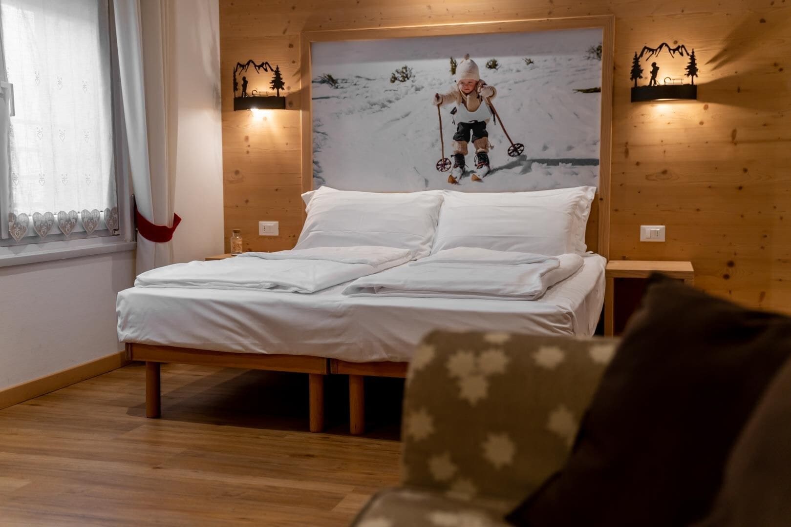 A wooden-paneled room with a bed, a nightstand, and a wall-mounted artwork depicting a skier.