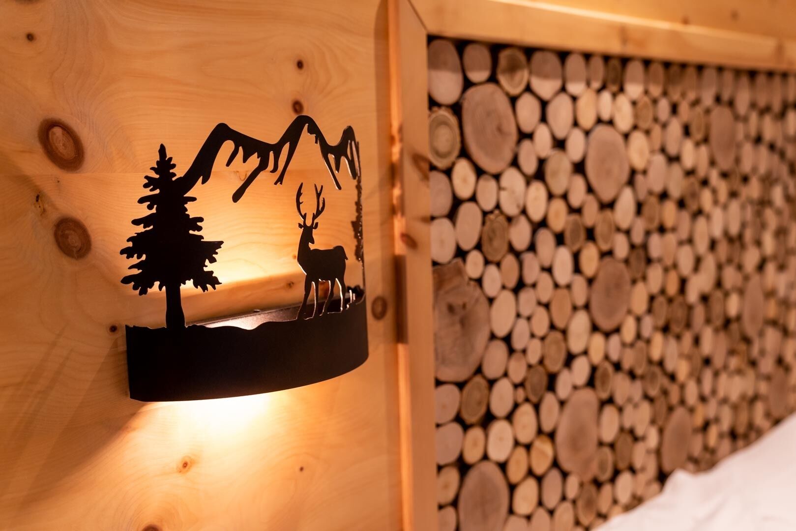 Een houten wand met een silhouet van een hert en een boom, en een stapel houtblokken.