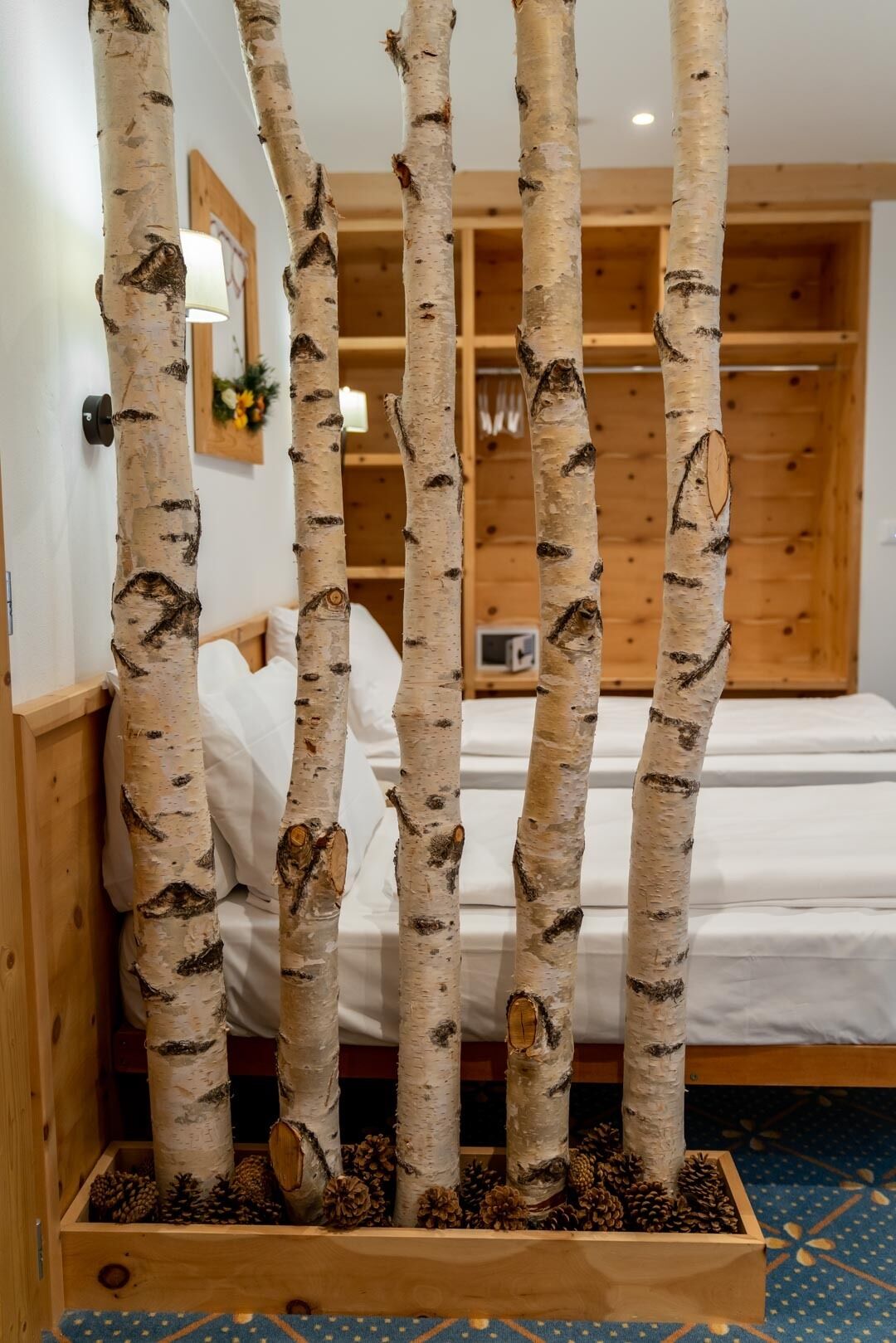 A room with birch tree decorations, a bed, wooden walls, and a blue patterned carpet.
