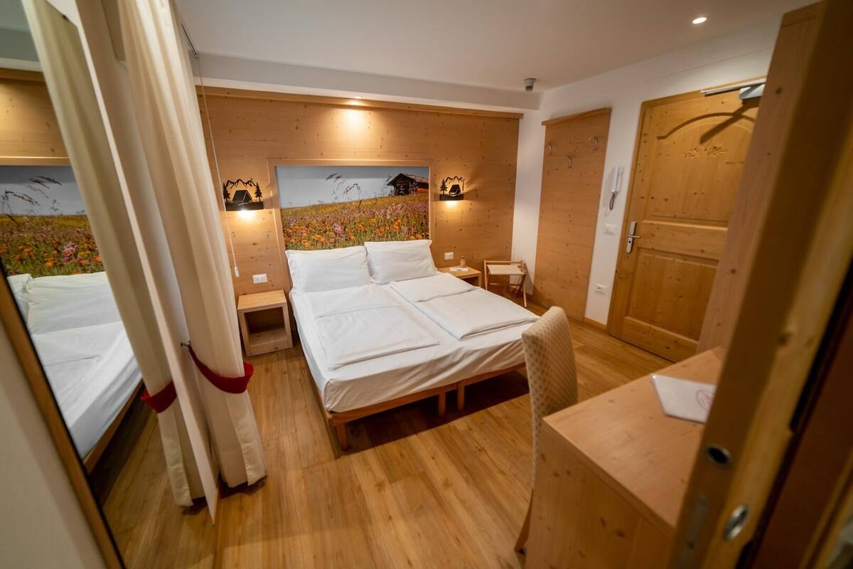 Un dormitorio con piso de madera, una cama con ropa blanca, una mesita de noche pequeña y un aplique de pared.