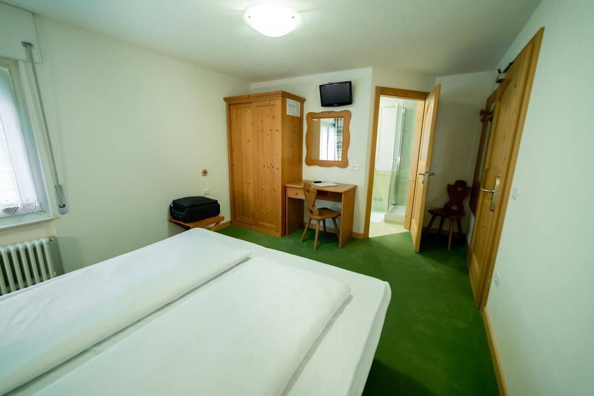 Un dormitorio con cama, escritorio, silla, televisor y armario.
