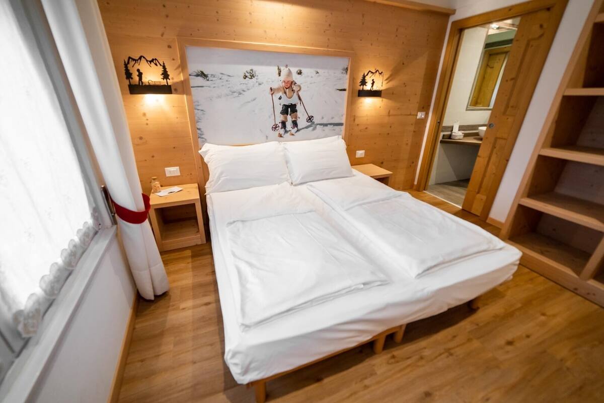 Un dormitorio acogedor con cabecera de madera, cama con ropa blanca, dos mesitas de noche e iluminación en la pared.
