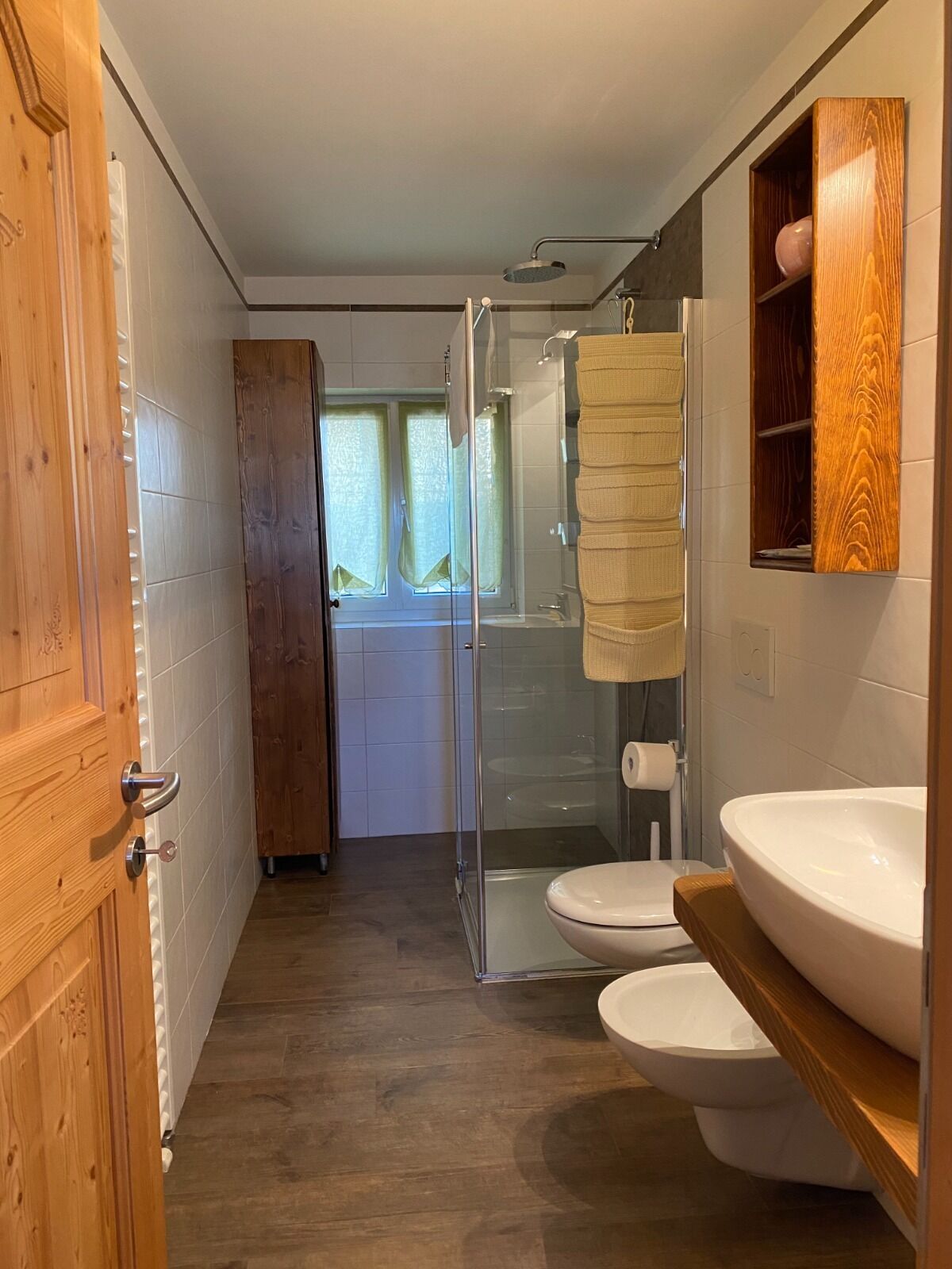 Un baño con cabina de ducha de vidrio, una puerta de madera, un lavamanos blanco y un inodoro.