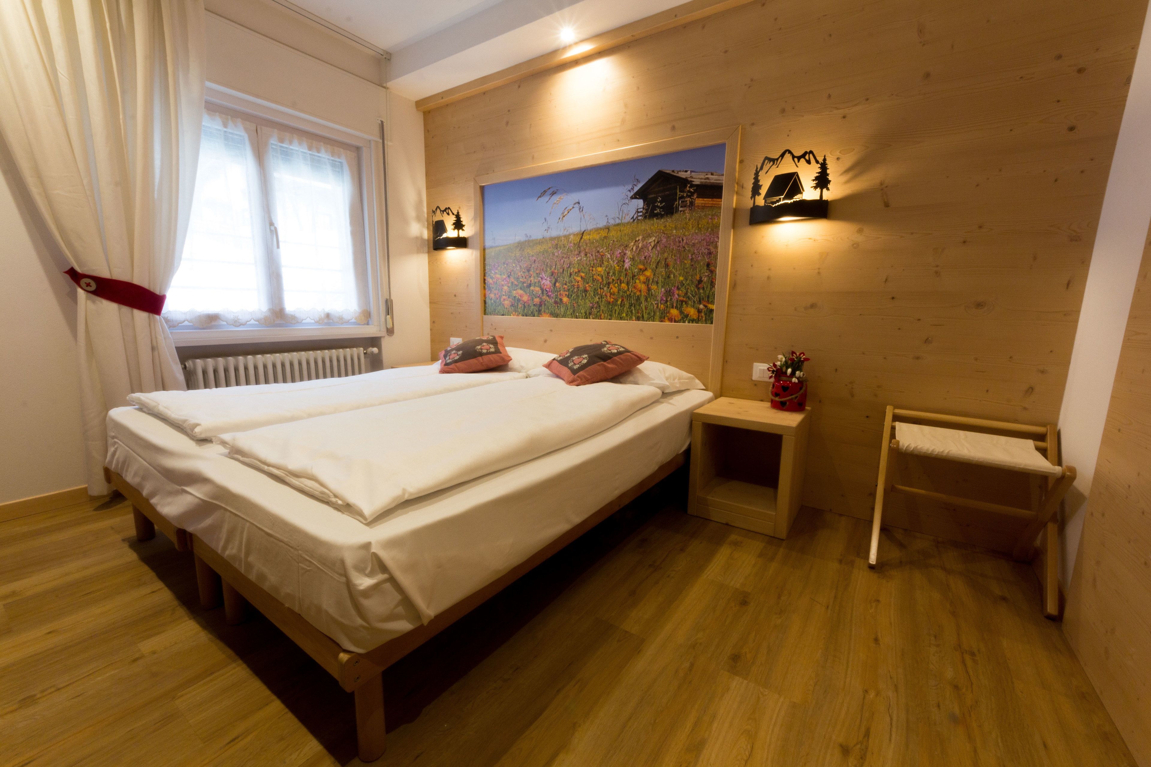 A double bed with white linens, a bedside table with a lamp, and a wall-mounted picture of a mountain landscape.