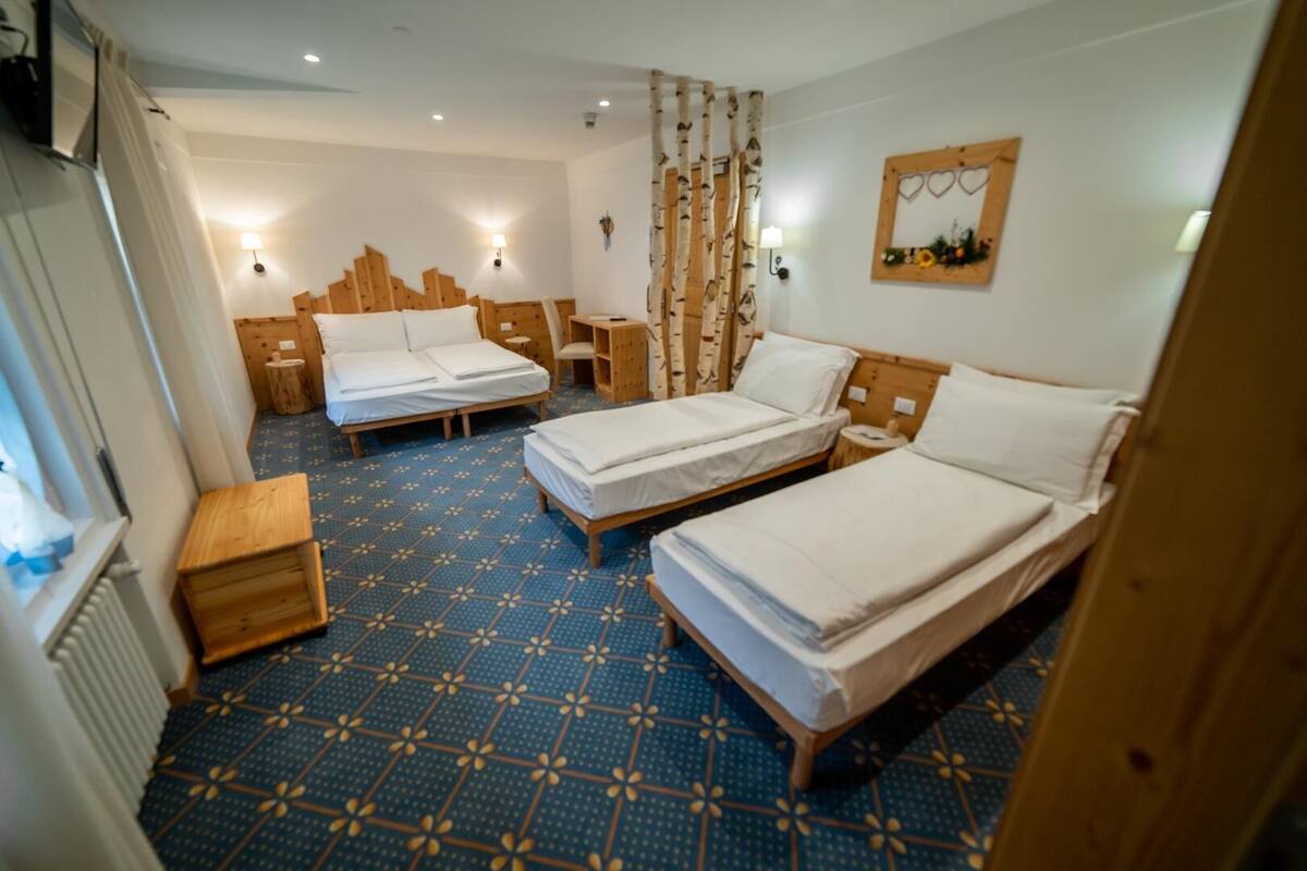 Habitación de hotel con dos camas individuales, cabecero de madera, una mesita pequeña de madera y una alfombra azul estampada.
