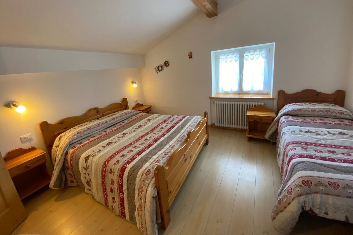 Un dormitorio con dos camas de madera, una ventana con cortinas, un radiador y una lámpara fijada a la pared.