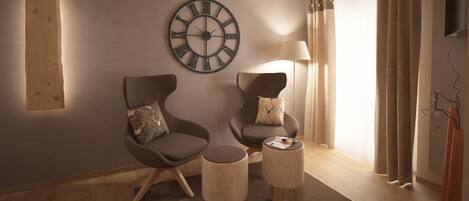 A modern living room with two armchairs, a round wall clock, a floor lamp, and a small table with magazines.