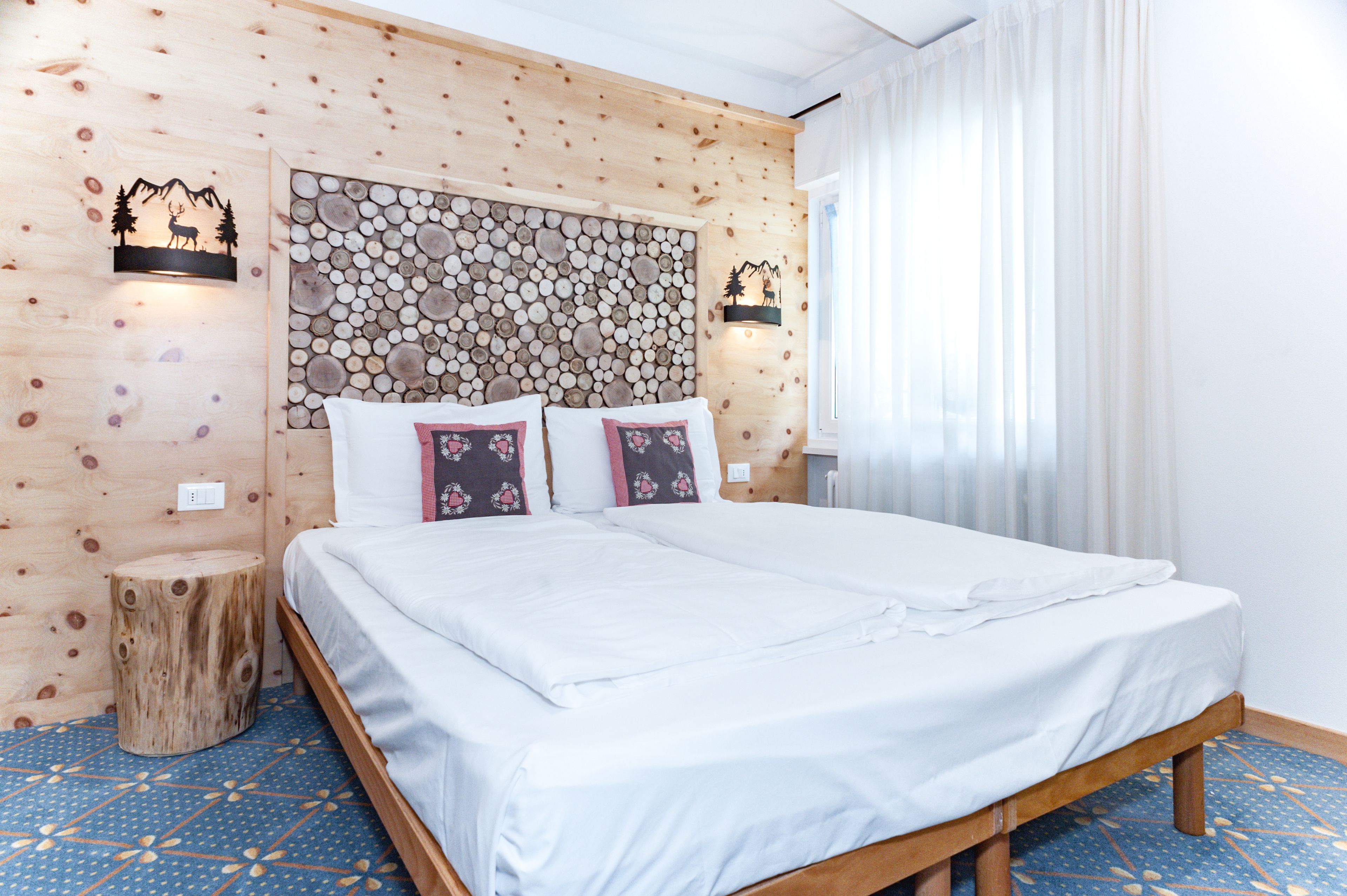 Una habitación con paneles de madera, una cama, un adorno mural de madera tallada y un taburete pequeño.