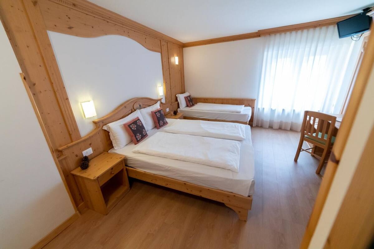 Una habitación con dos camas de madera, una silla de madera y una mesita.
