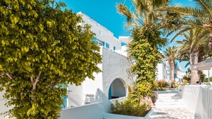 A courtyard with white buildings, a stone floor, and greenery. - Hotel Sagterra (Naxos)