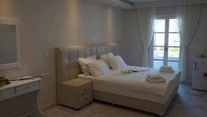 A bedroom with a large bed, bedside tables, a dresser, and a window with curtains. - Hotel Sagterra (Naxos)
