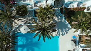 An aerial view of a resort with a central swimming pool surrounded by palm trees and a patterned walkway. - Hotel Sagterra (Naxos)