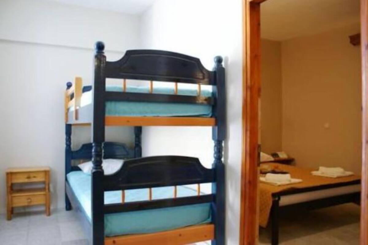Um quarto com uma cama de solteiro e beliche, uma pequena mesa de cabeceira de madeira e uma mesa com uma cadeira.