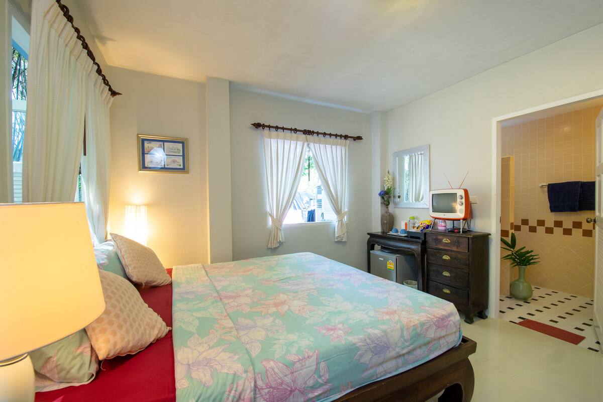 Un dormitorio con cama, cómoda, televisor y baño visible a través de una puerta abierta.