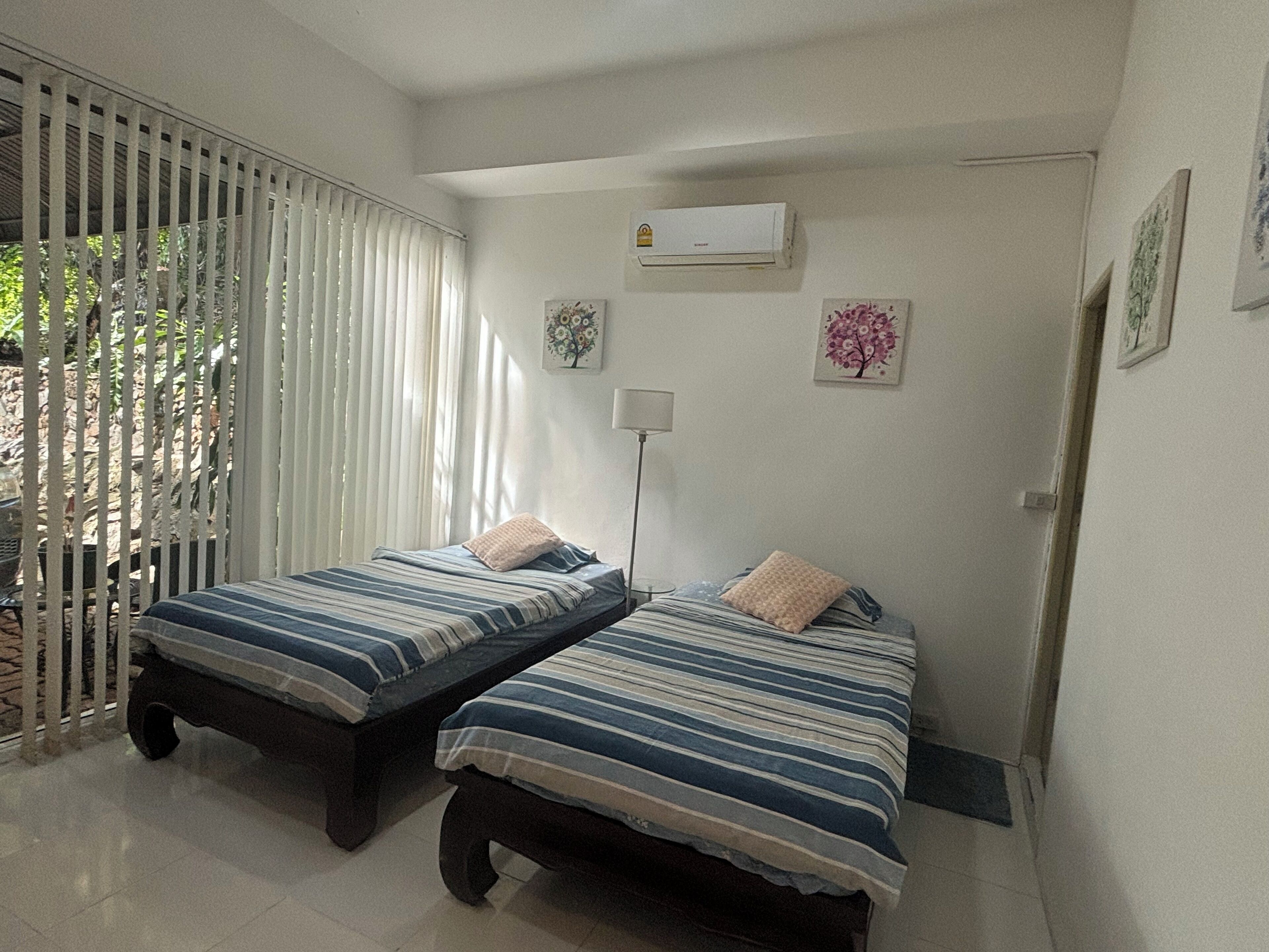 Une chambre avec deux lits, une fenêtre avec des stores, un appareil de climatisation et une porte.