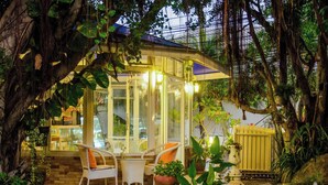 Un patio vitré, aménagé avec des chaises en osier blanc et une petite table, entouré de plantes en pot et de rochers.