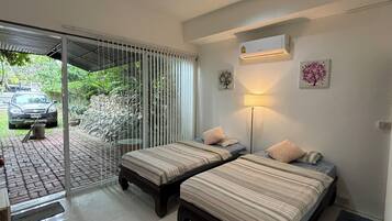 A room with two beds, a ceiling fan, a wall-mounted air conditioner, and a view of a parked car outside.