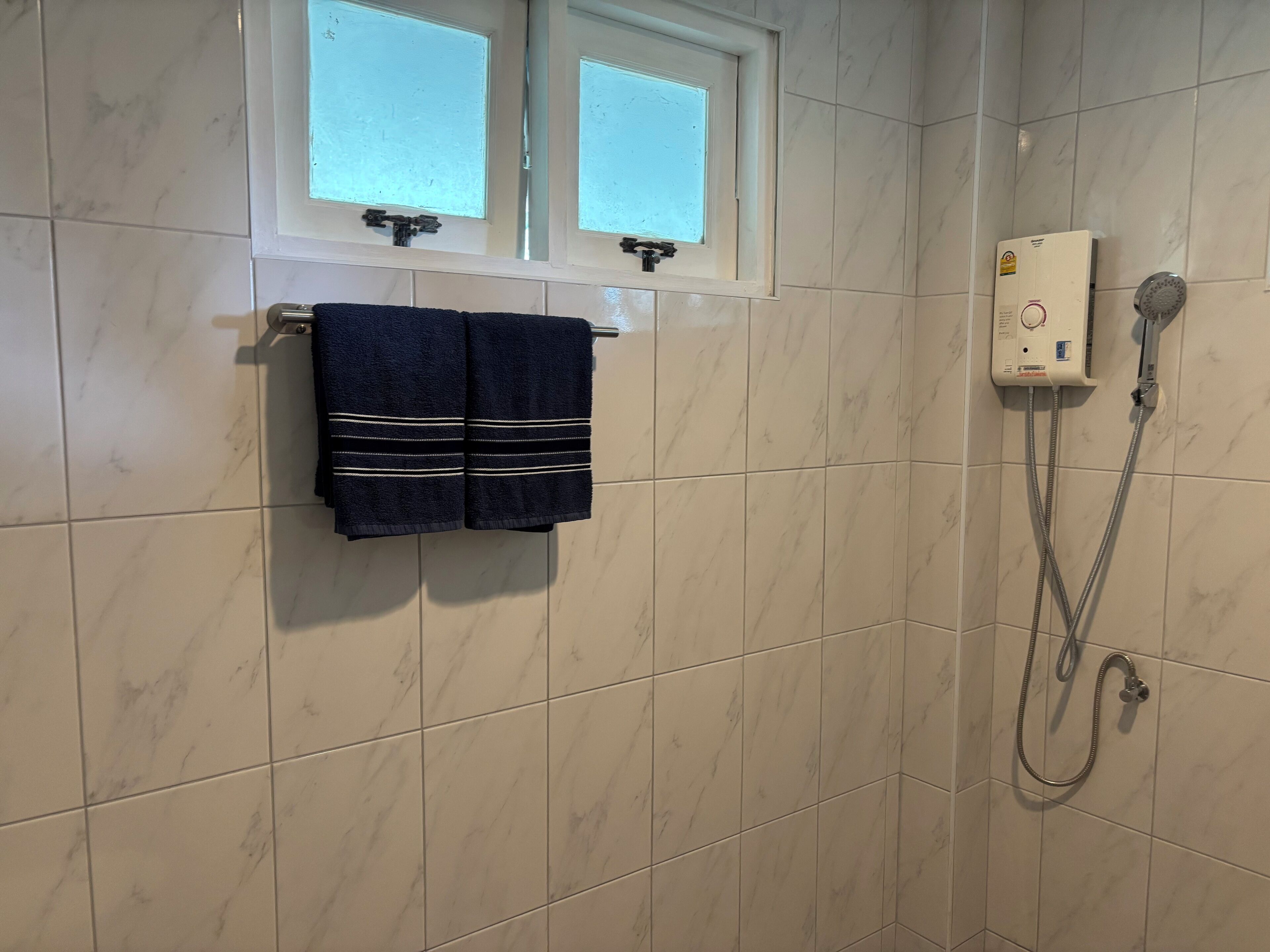 Un baño con ducha, un tendedero de toallas con dos toallas y un ventanal sobre la ducha.