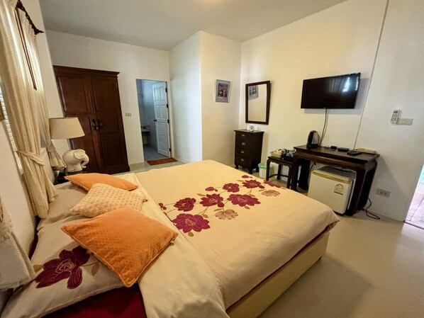 A bedroom with a bed, a dresser, a desk, a television, and a door leading to another room.