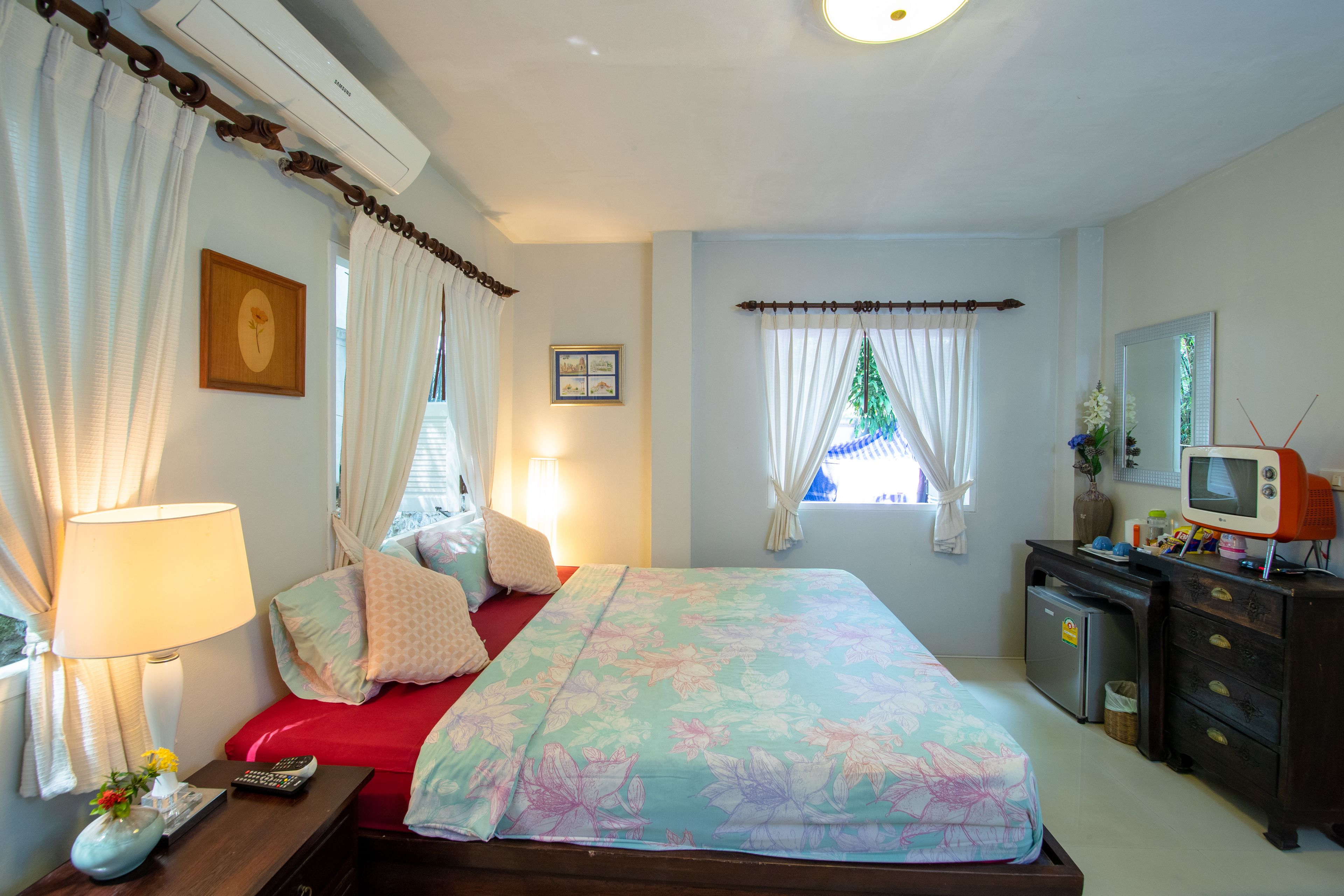 Een slaapkamer met een bed, een dressoir, een televisie en een raam met gordijnen.