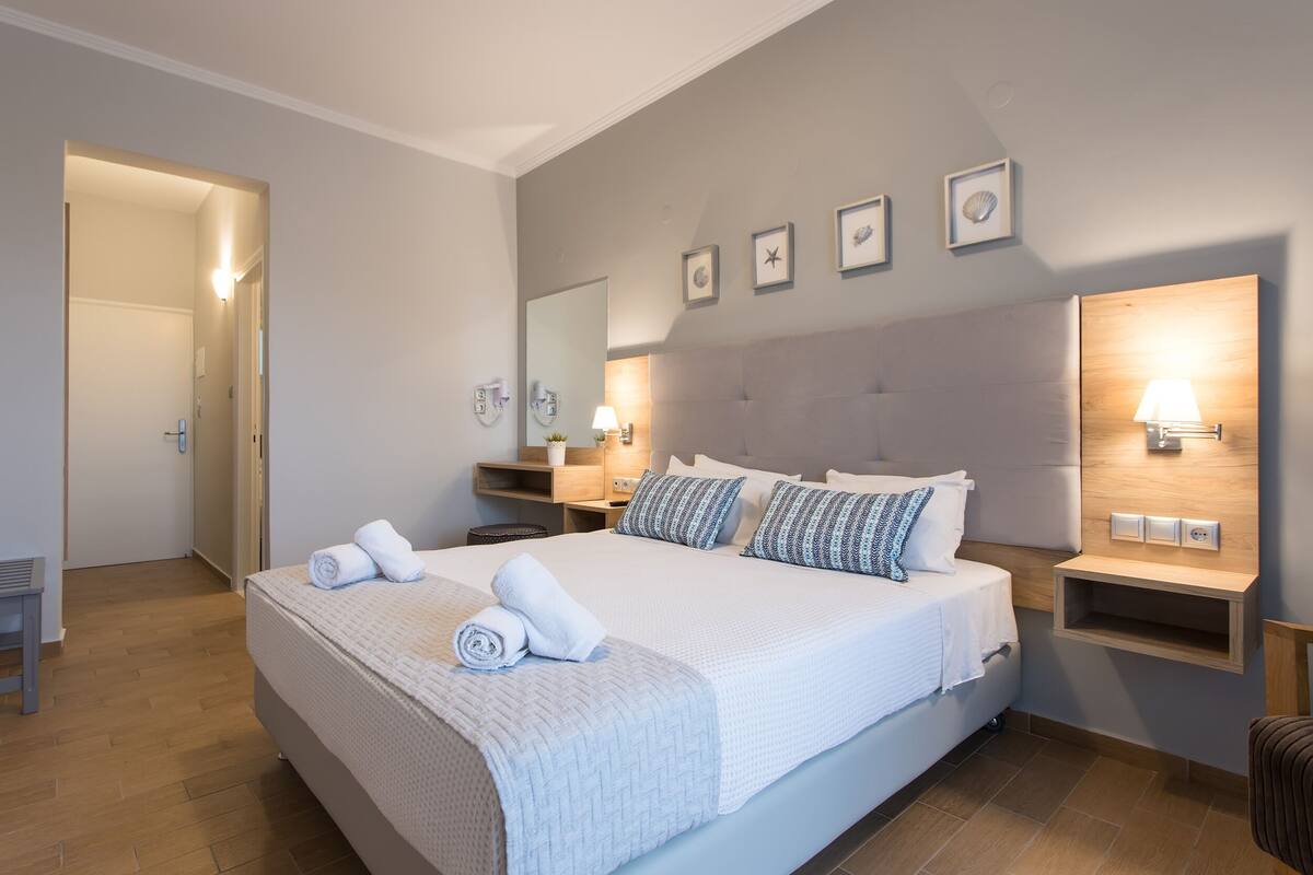 Quarto de hotel moderno com uma cama grande, mesas de cabeceira, um espelho e luminárias fixadas na parede.
