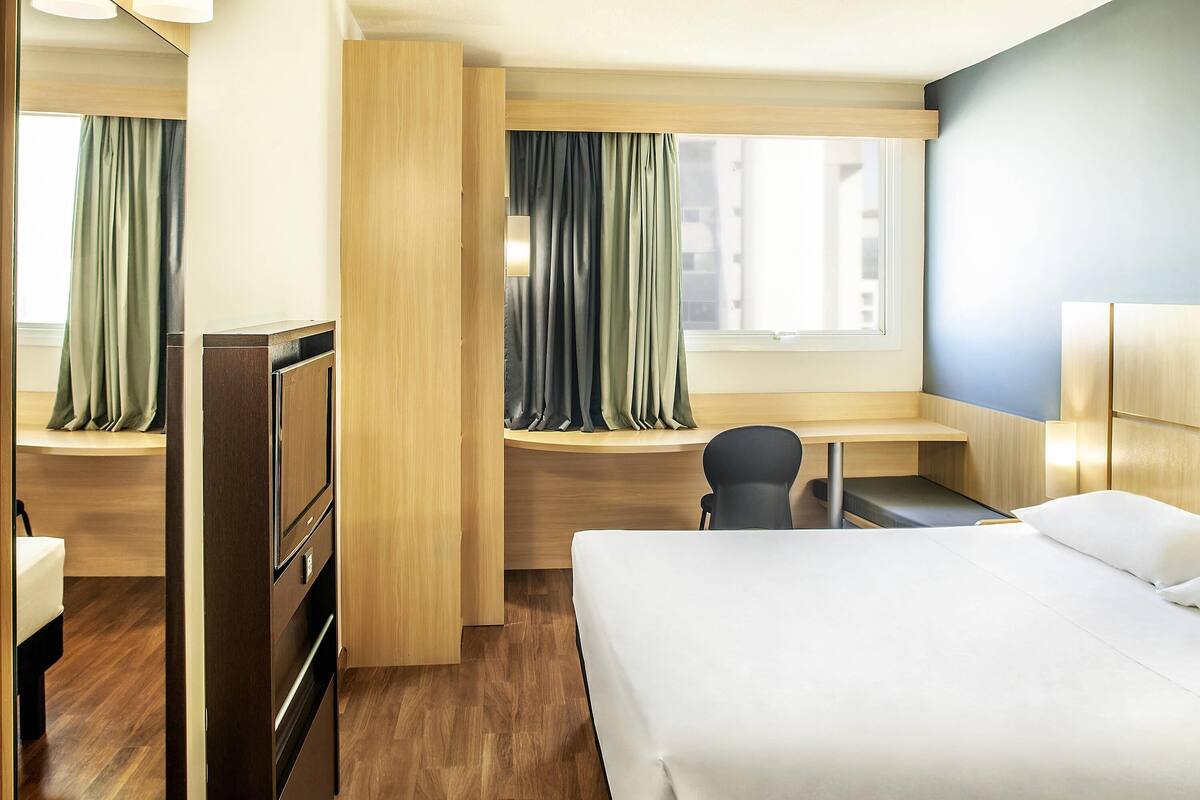 A hotel room with a bed, desk, chair, and a window with curtains.