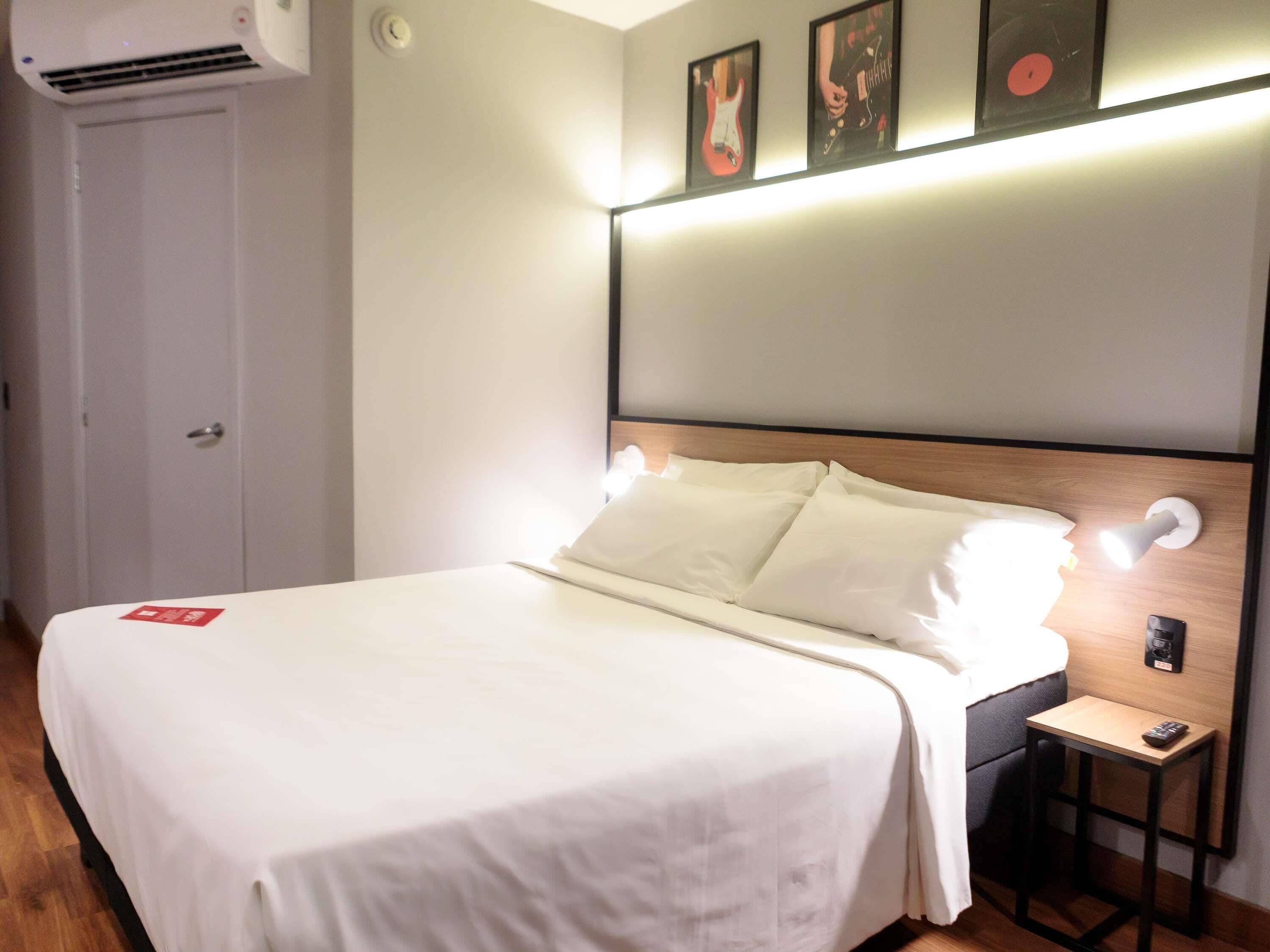 Una habitación de hotel con cama, mesita de noche y lámpara de pared.
