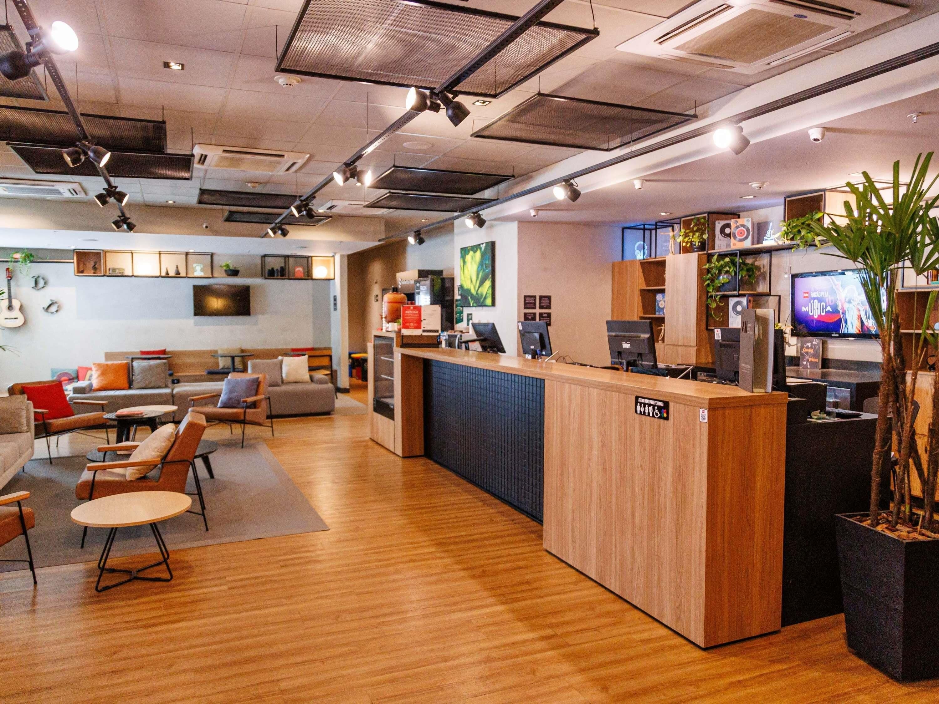 A modern hotel lobby with a reception desk, seating area, and a television screen.