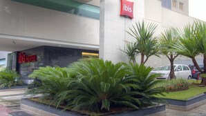 A modern hotel entrance with a prominent red sign, lush green landscaping, and a parking area. - Ibis Belo Horizonte Savassi (Belo Horizonte)