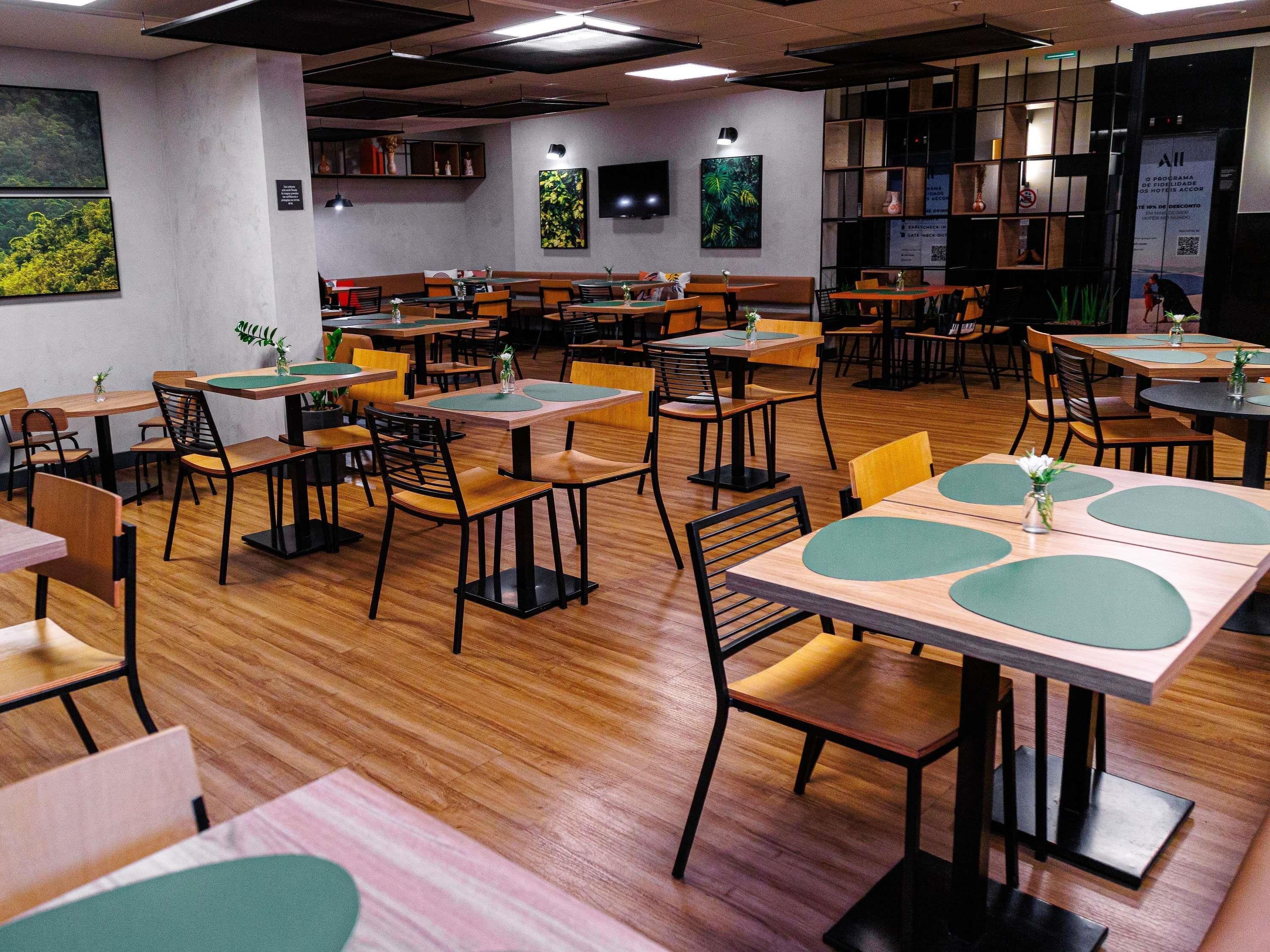 A restaurant with multiple tables and chairs, wooden flooring, and wall-mounted artwork.