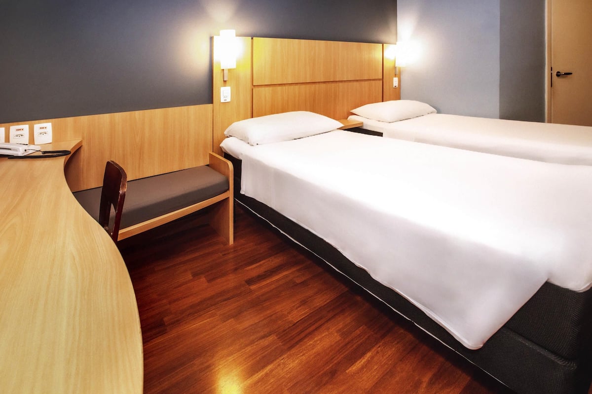 A hotel room with two beds, a desk, a chair, and a wooden headboard.