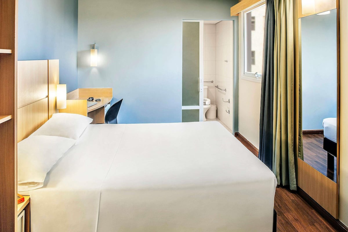 A hotel room with a bed, bedside table, lamp, and a view of the bathroom.